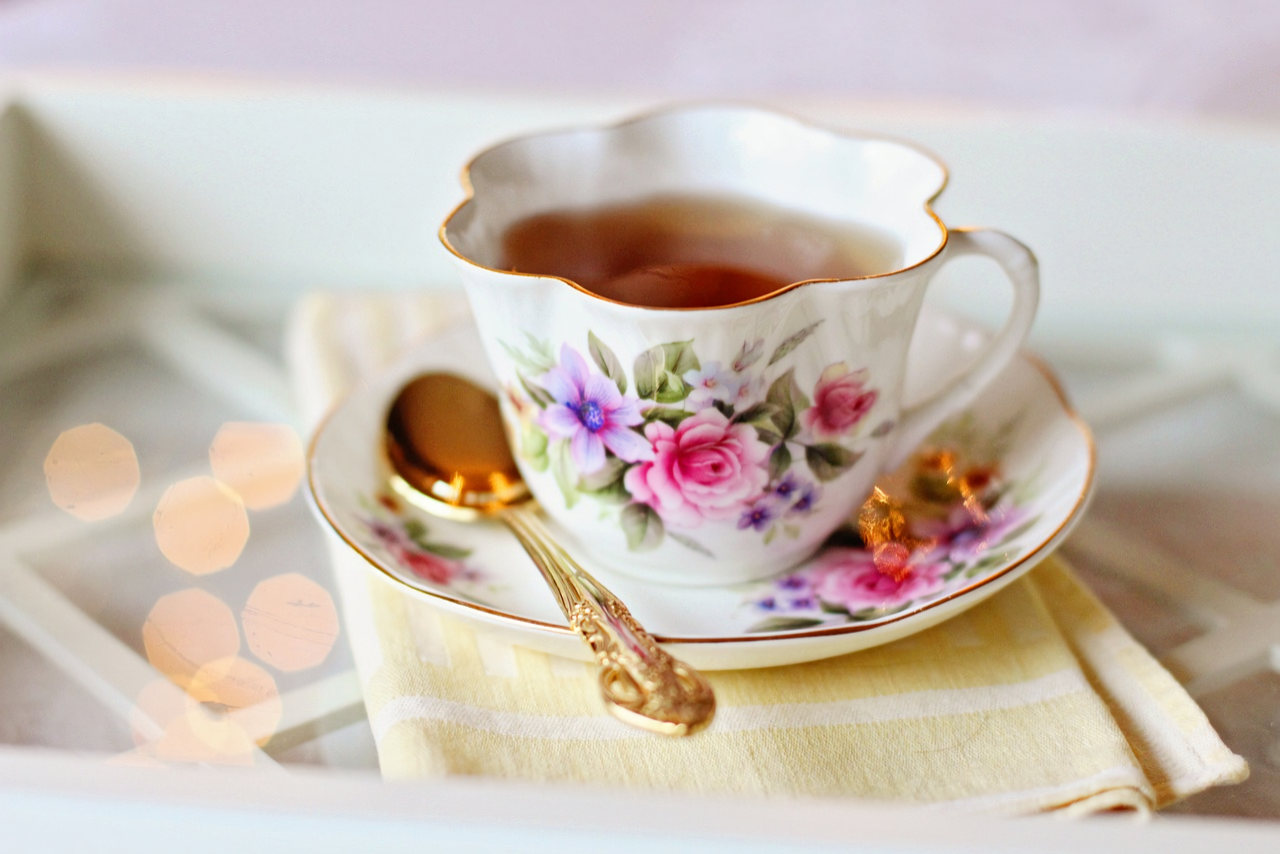 A fancy teacup with a floral pattern sits on a matching saucer, along with a gold spoon